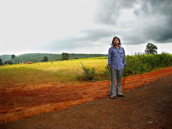 Young man standing by agricultural field against cloudy sky