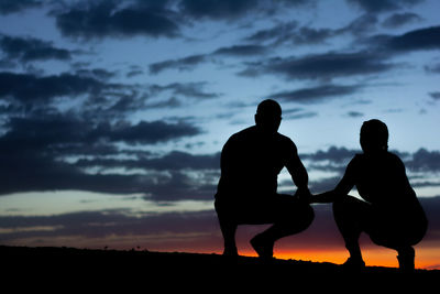 Silhouette friends standing on land against sky during sunset