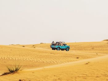 People traveling in off-road vehicle on desert against sky during sunny day