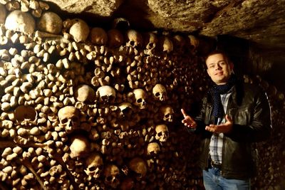 Portrait of young man standing against skulls on wall