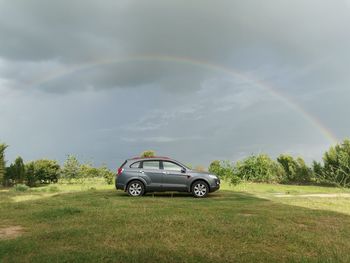 Car on field against rainbow in sky