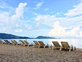 Empty chairs on beach against cloudy sky