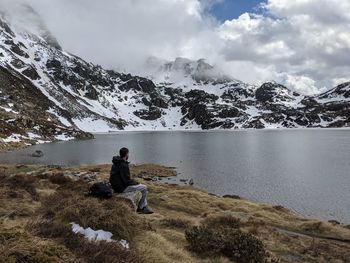 Rear view of man sitting on mountain against sky