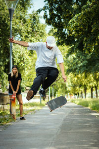 Couple performing stunts on skateboard on footpath at park