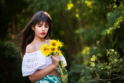 Woman holding sunflowers while standing on field