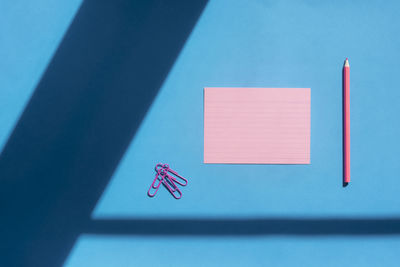 Directly above shot of paper clips with paper and colored pencil on blue table