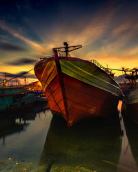 Boat moored at harbor against sky during sunset