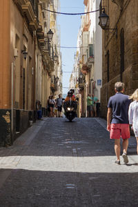 Rear view of people walking on street amidst buildings in city