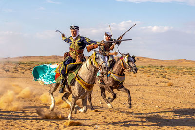 Rear view of man riding camels on field against sky