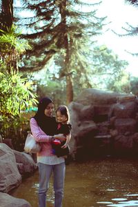 Mother and daughter standing on rock by tree