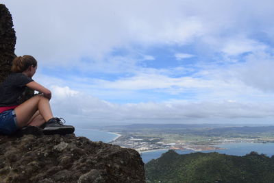 Man sitting on rock by sea against sky