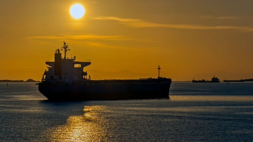 Silhouette ship at harbor against sky during sunset