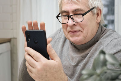 Hoary old man looking at web camera, holding phone, talking with children, wife online. senior