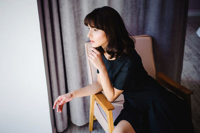 Beautiful young woman sitting on chair at home