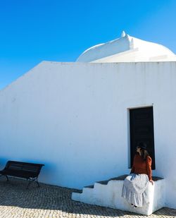 Rear view of people sitting outside building against blue sky