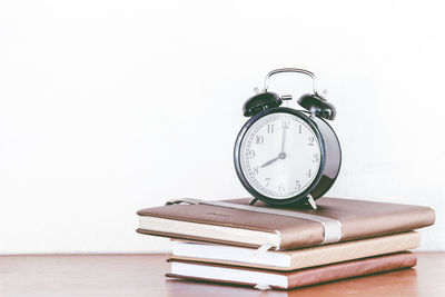 Alarm clock on books over table against white background
