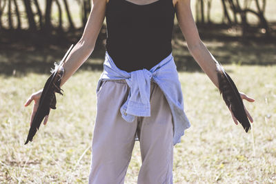 Midsection of woman with feathers standing on field during sunny day