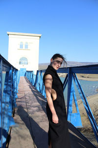 Young woman standing against built structure against clear blue sky