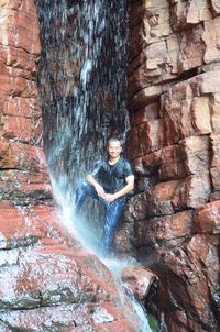 Man enjoying waterfall amidst rock formations in forest