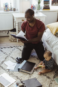 Male entrepreneur kneeling while reading diary by son at home