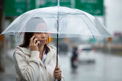 Mid adult woman with umbrella talking over smart phone in city