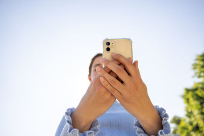Midsection of woman using mobile phone against sky