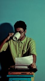 Young man drinking coffee while sitting against blue wall