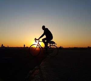 Silhouette man riding bicycle at sunset