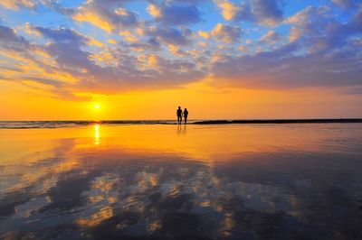 Silhouette couple on beach against sky during sunset