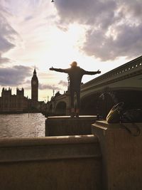 Man sitting on bridge in city against cloudy sky