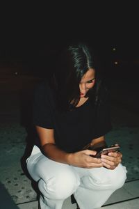 Young woman using mobile phone while sitting in the dark