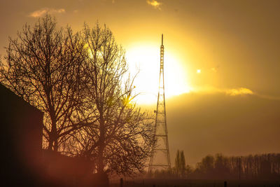 Low angle view of communication tower and trees against sky during sunset