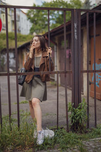 Woman holding camera while standing against plants