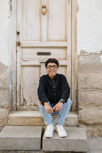 Young transgender man posing sitting on the front steps of a house.