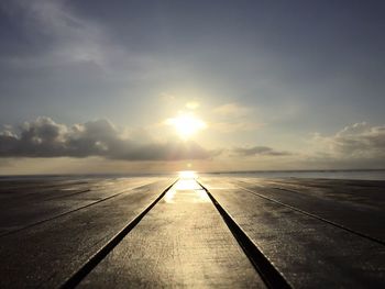 Wooden dock by sea against sky during sunrise