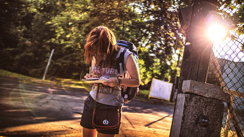 Woman writing in book while standing on road