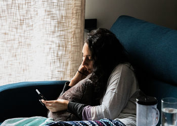 Woman using mobile phone while sitting on sofa at home
