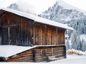 Wooden hut by snowcapped mountains against sky during winter