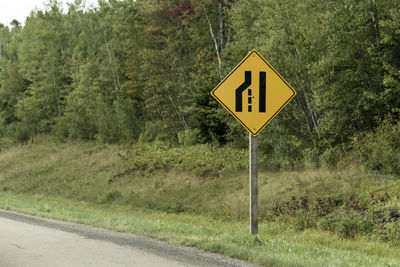 Road sign by trees on field