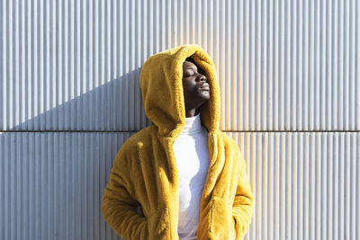 Young african man in yellow jacket with hands in pockets against white wall