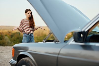 Side view of smiling young woman standing against car