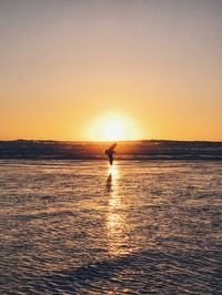 Silhouette person standing in sea against clear sky during sunset