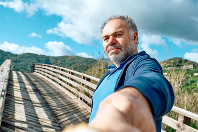 Follow me. man holds and pulls photographer's hand and leading her on wooden bridge in rural nature.