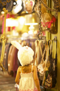 Rear view of girl wearing hat standing in illuminated market during christmas