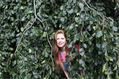 Portrait of smiling young woman hiding behind green leaves