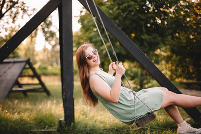 Happy young woman swinging in park during summer