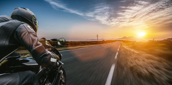 Man riding bicycle on road against sky during sunset