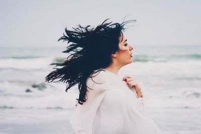 Side view of beautiful woman with tousled hair standing at beach