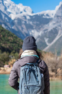 Rear view of woman standing by lake against mountains