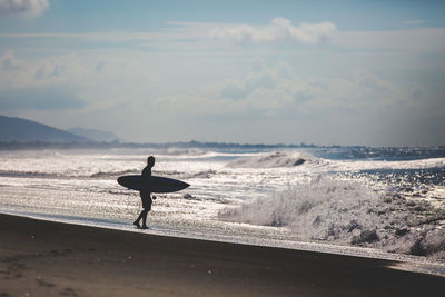 Silhouette of surfer on beach against sky